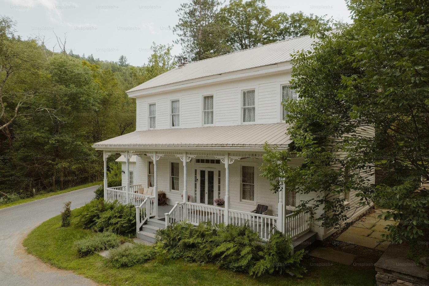 White farmhouse with a porch surrounded by trees